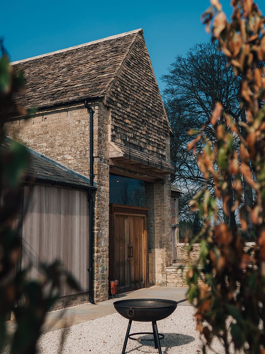 Ivy Lodge restored Cotswolds stone barn exterior with slate roof, oak door, and fire pit on gravel terrace